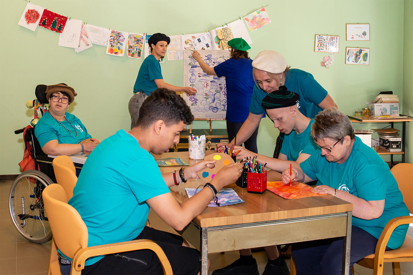 Gruppo al tavolo di un laboratorio creativo dipinge e colora in una sala verde con i disegni appesi