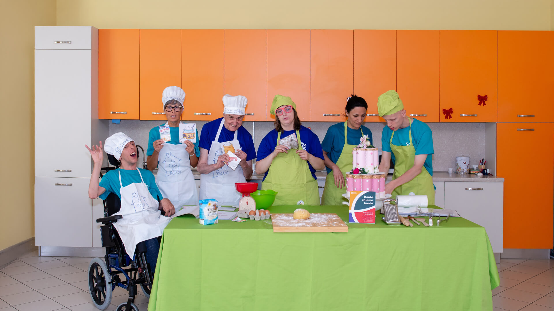 Sei persone con cappelli da cuoco e grembiuli dietro un tavolo da cucina con torta decorata