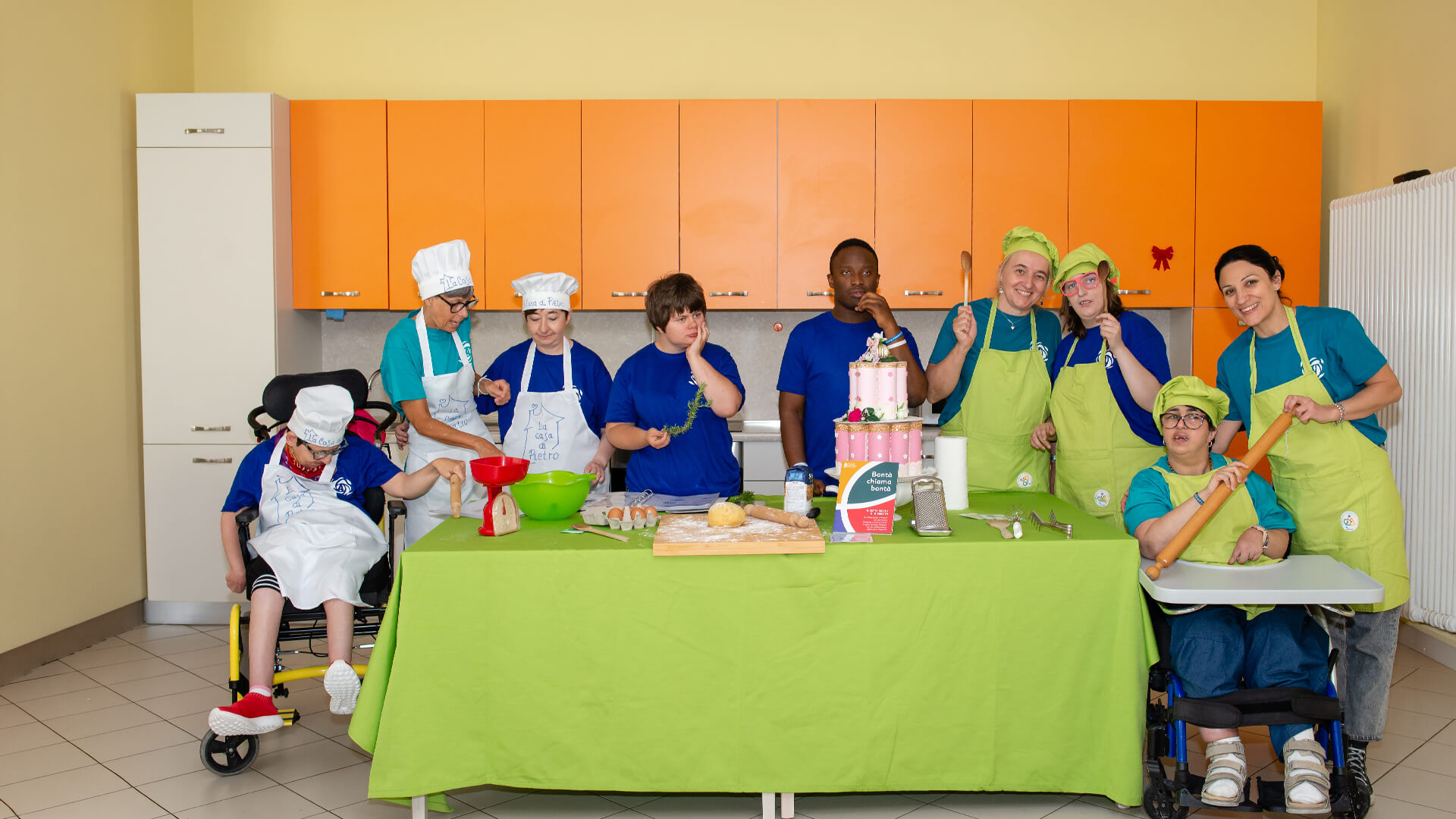 Gruppo numeroso con grembiuli e cappelli da cuoco prepara impasti e dolci in una cucina attrezzata